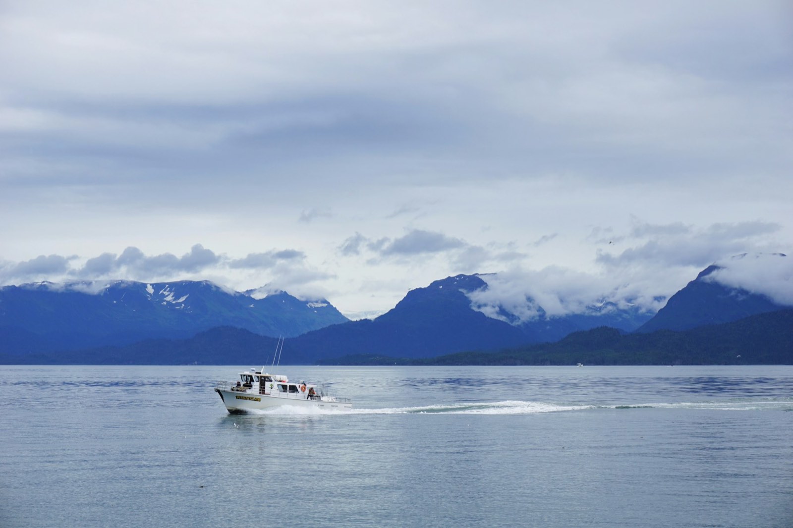 A charter boat running below cloud-wrapped coastal mountains