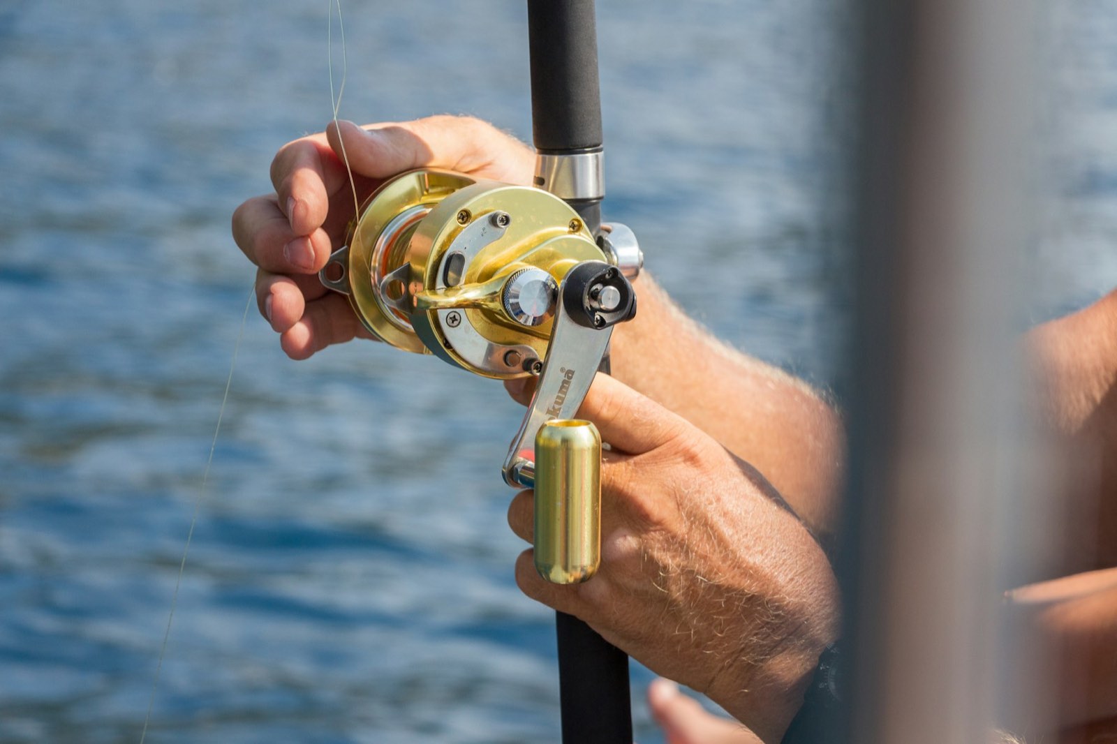 A trolling reel in an angler's hands over blue water