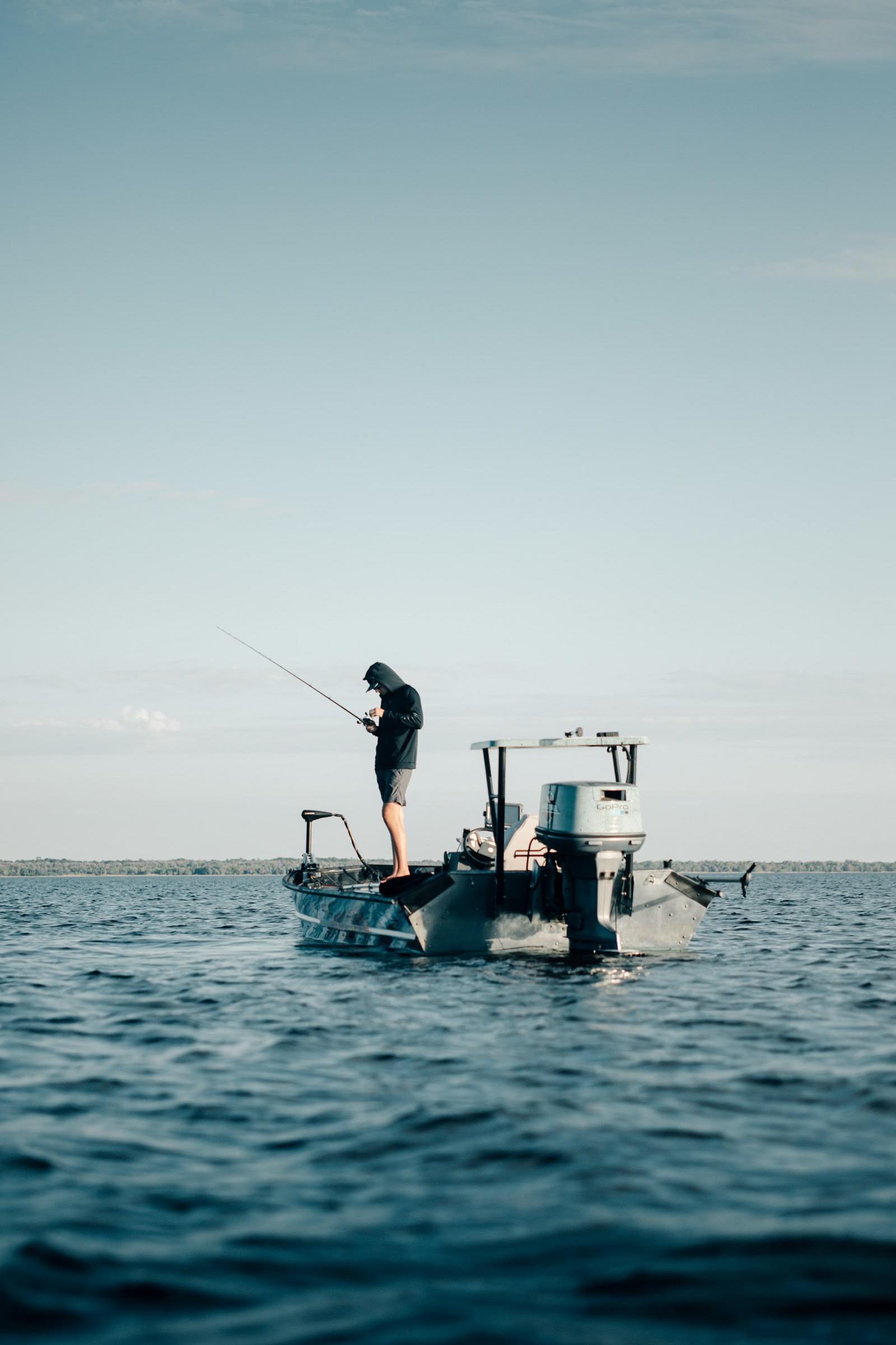 An angler working a rod from the deck of a boat on calm water